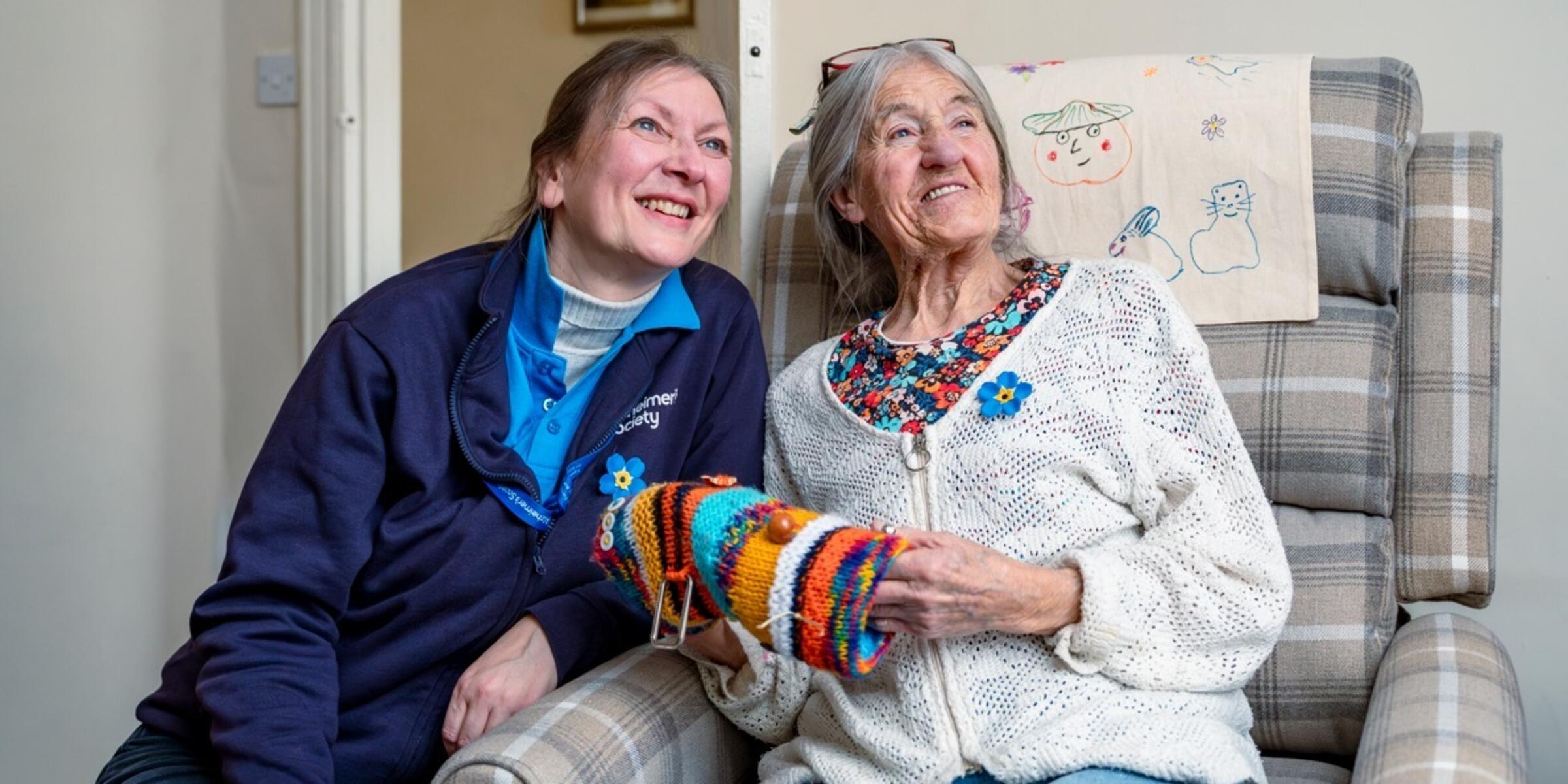 Smiling Kathy sat in an armchair and Dementia Adviser Helen leaning into the chair