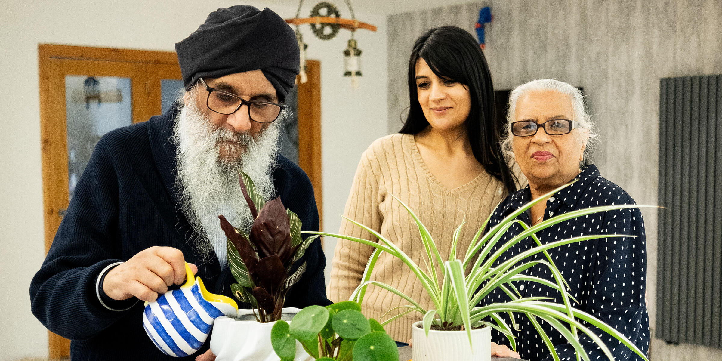 Harjit Singh Sagu watering houseplants, with his wife and daughter beside him