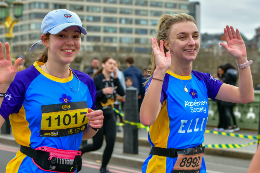 Two Alzheimer's Society runners smile and wave as they take part in race