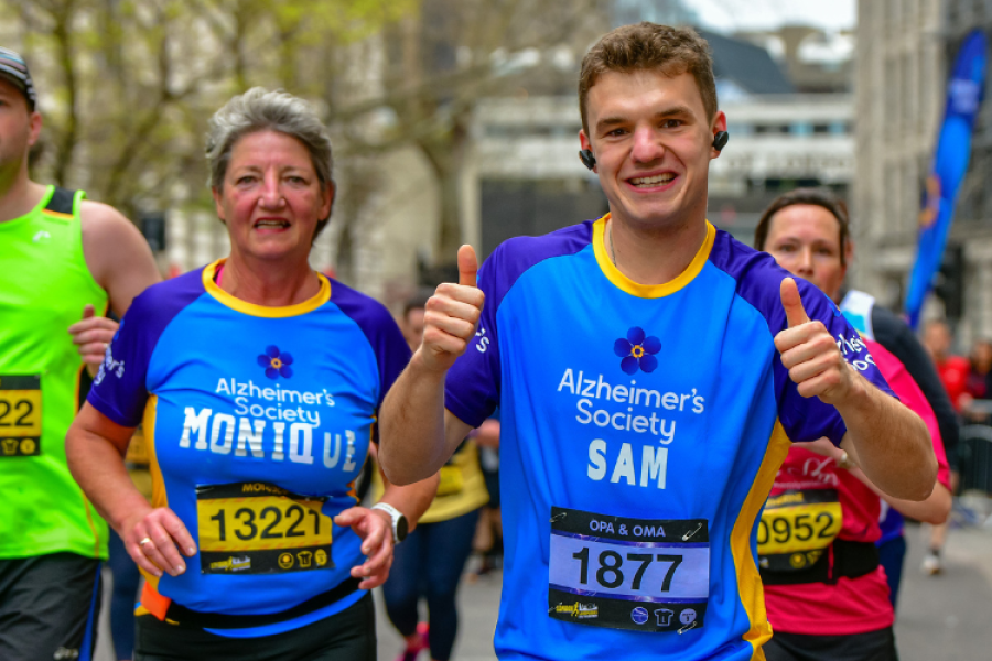Two Alzheimer's Society runners competing, both smiling and one is giving two thumbs up
