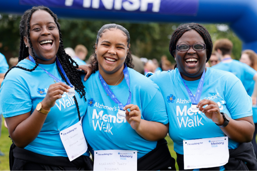 3 women smiling at the finish line, wearing blue Memory Walk t-shirts and medals
