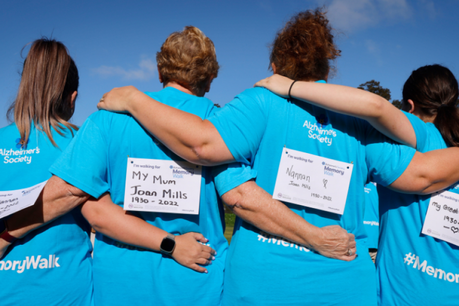 4 women arm in arm with their backs to camera, wearing blue Memory Walk t-shirts