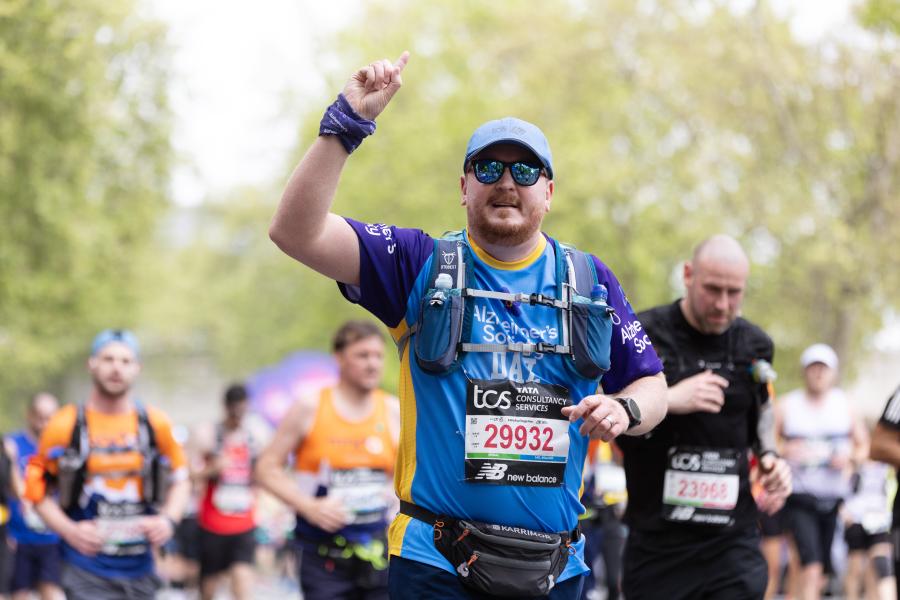 A runner waves while running along the London Marathon route. 