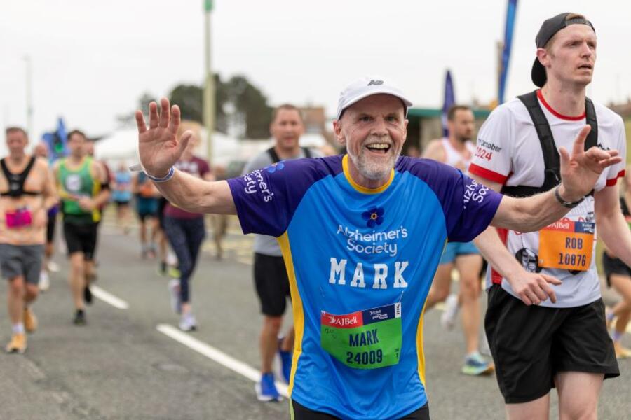 A man in an Alzheimer's Society running top raises his arms while running