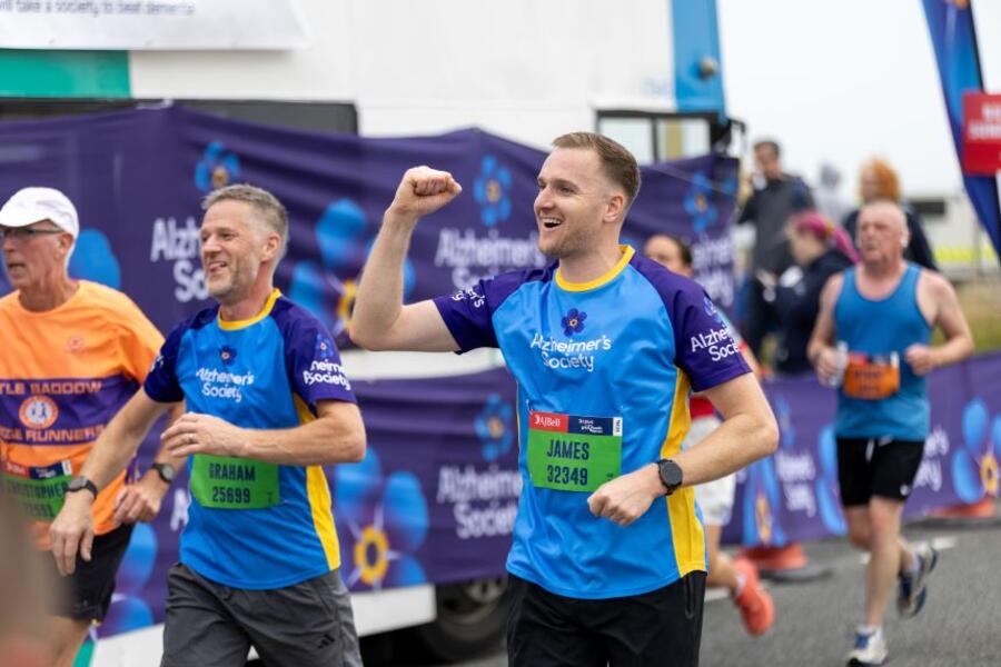 Two male runners in Alzheimer's Society branding, one is punching the air