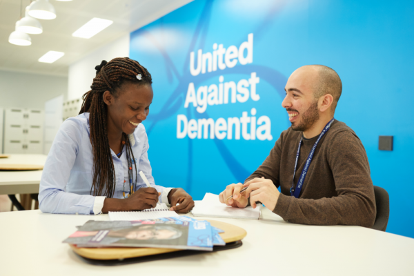 Two Alzheimer's Society employees having a meeting in front of wall that says 'United Against Dementia'