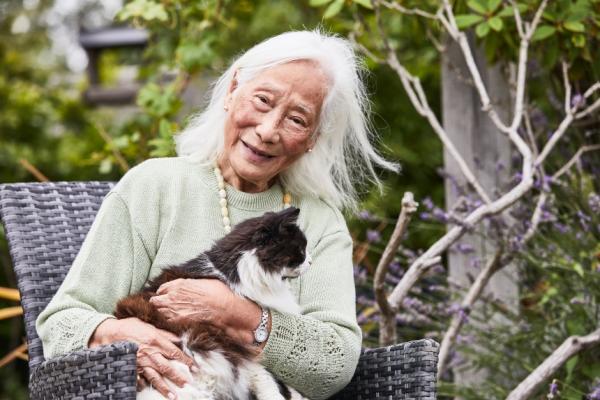 An older woman holding a cat while sitting in a garden chair
