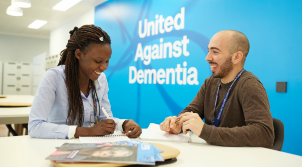 Two Alzheimer's Society employees having a meeting in front of wall that says 'United Against Dementia'