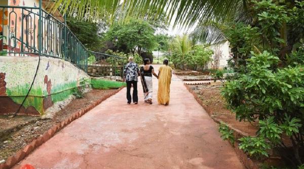 Three women walking on a clay path surrounded by trees in Rural India
