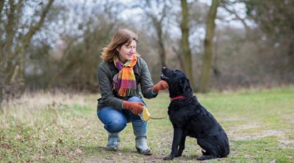 A woman in a park kneeling down to pet her black dog