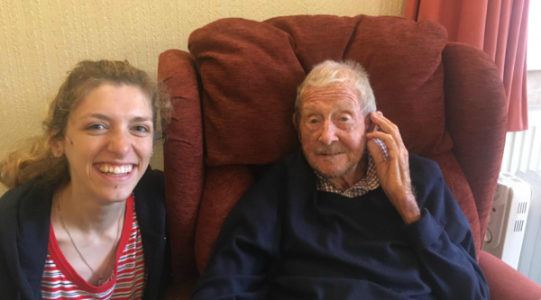 Ruby smiling beside her granddad, George, who is sitting in a red armchair