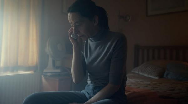 A woman sitting on her bed in a dark room talking on the phone