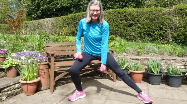 Jane demonstrating a side lunge while holding weights in the outdoors