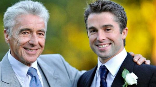 Charlie and his dad Nigel at a wedding, both wearing suits and smiling. Nigel's arm is around Charlie's shoulder.