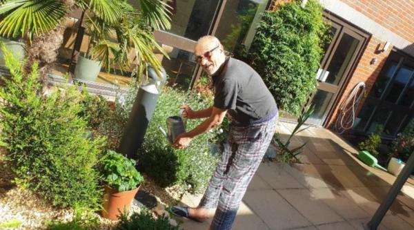 Deepak at the care home holding a watering can while outside in the care home's courtyard