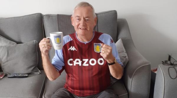Peter wearing an Aston Villa shirt and holding a AVFC mug, smiling and with a clenched fist in excitement