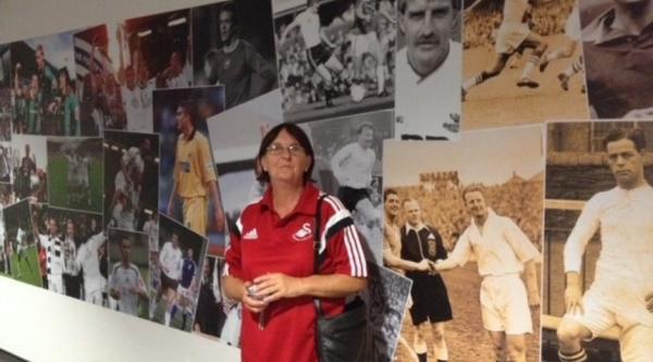 Sue in front of a wall covered with photographs of footballers, on the Swansea City stadium tour