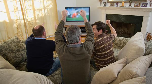 Three men celebrating a football goal in a living room