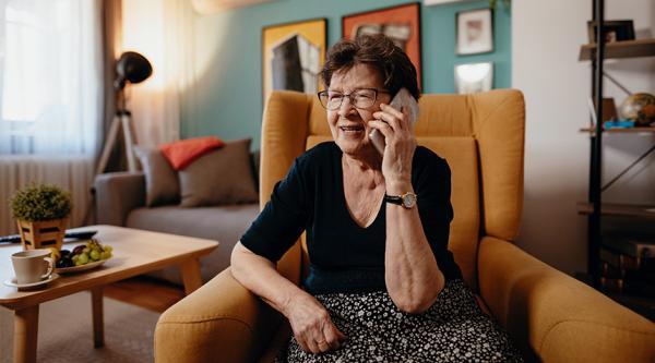 A woman sits in an armchair smiling, she's making a call on her mobile phone.