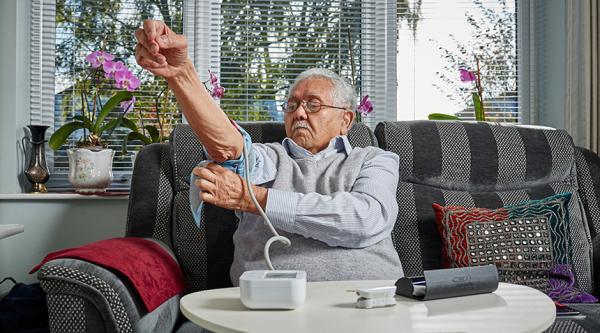 A person affected by dementia checks their blood pressure at home on their sofa