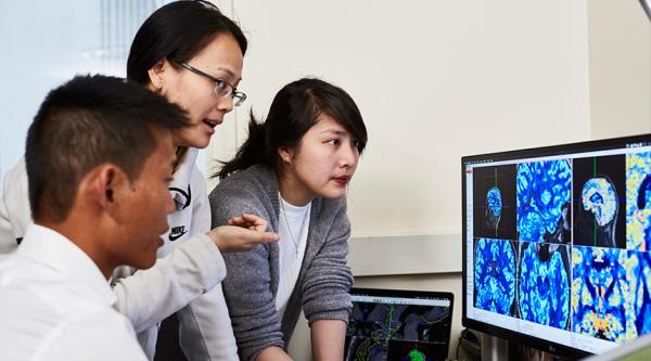 Three researchers assess scans on a screen