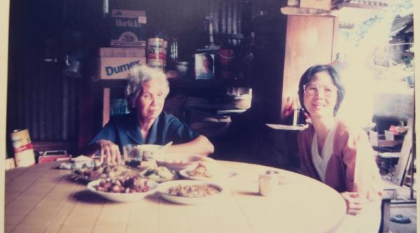 Two women sit around a table with food in a vintage photo