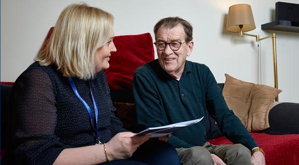 A man and a woman sit on a sofa looking at an Alzheimer's Society publication