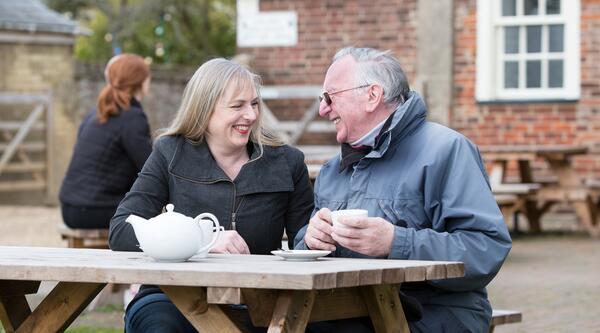 A couple sitting on an outdoor restaurant bench smiling at each other