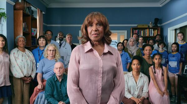 A woman standing in her living room surrounded by her family, doctors and dementia advisers.