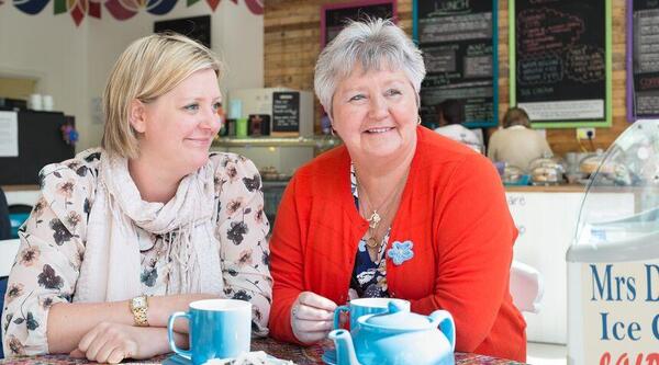 Two people sit in a cafe with mugs and a teapot