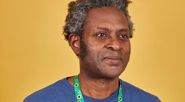 Man with grey and black curly hair wearing a blue t shirt and a sunflower lanyard