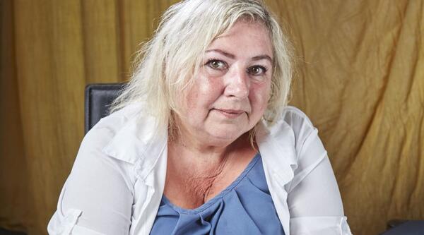 Anita Goundry sits down looking at the camera wearing a blue top and white shirt