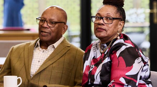 A man and woman sat at a table, the woman is looking at the camera