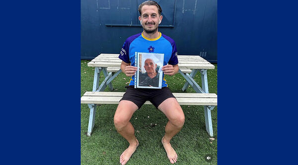 Phill has brown hair, he's sat down, wearing a blue Alzheimer's Society t-shirt and he's holding a picture of his grandad
