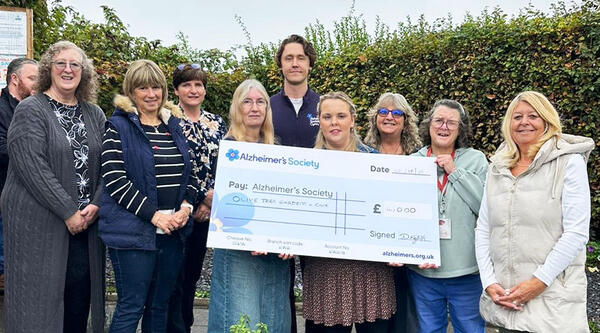 Volunteers from Olive Tree Cafe stood outside holding a big cheque.