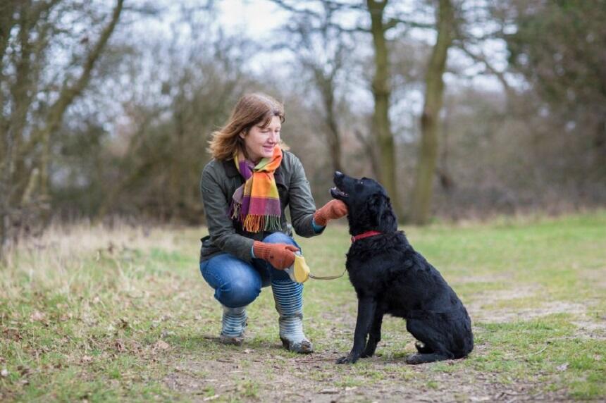A woman in a park kneeling down to pet her black dog