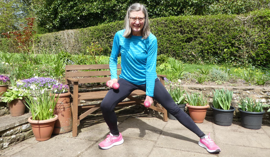 Jane demonstrating a side lunge while holding weights in the outdoors