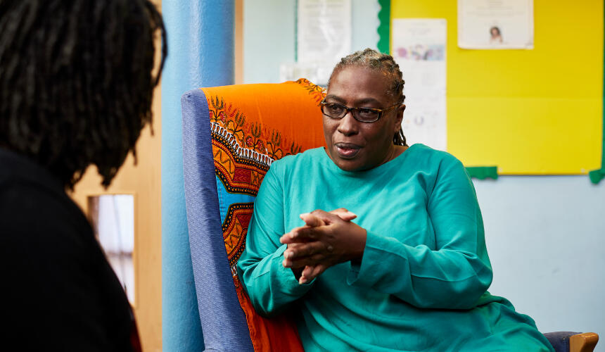 A Black woman in conversation with a person out of view, with her hands together and listening intently