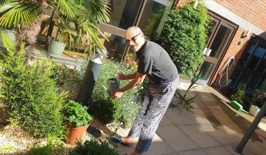 Deepak at the care home holding a watering can while outside in the care home's courtyard