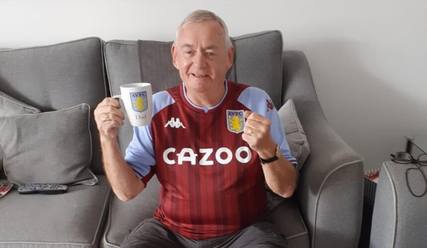 Peter wearing an Aston Villa shirt and holding a AVFC mug, smiling and with a clenched fist in excitement