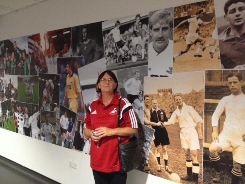 Sue in front of a wall covered with photographs of footballers, on the Swansea City stadium tour