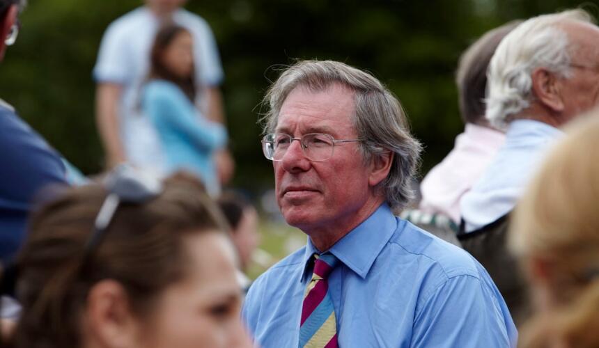 Tony is in a shirt and tie in the middle of a group of people, looking into the distance