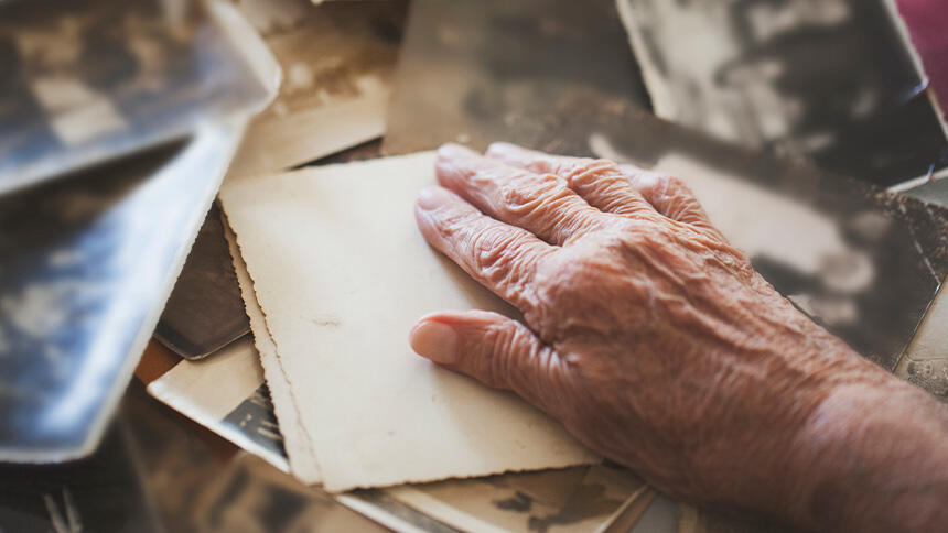 An older person's hand on top of some photographs, which are face down.
