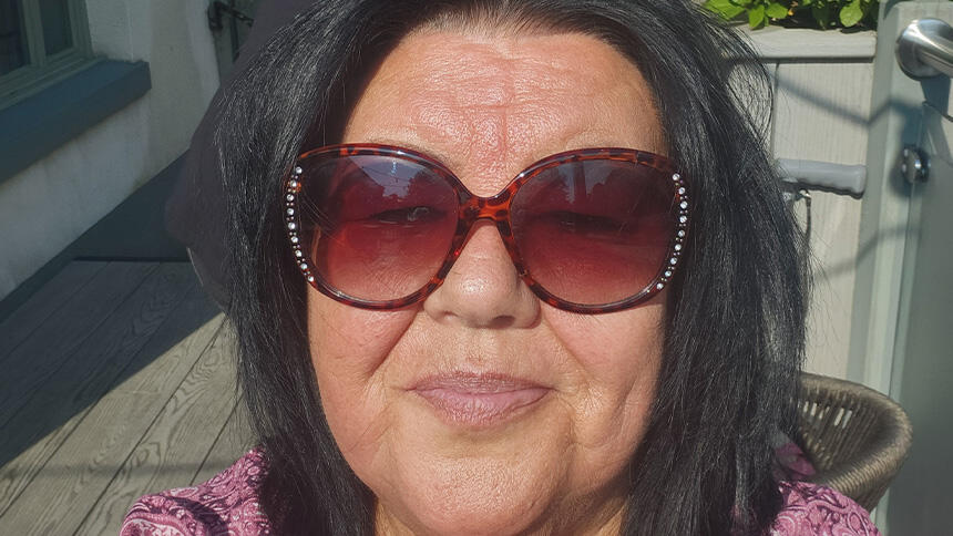 Carol Rimmer sat in sunshine wearing sunglasses and pink top