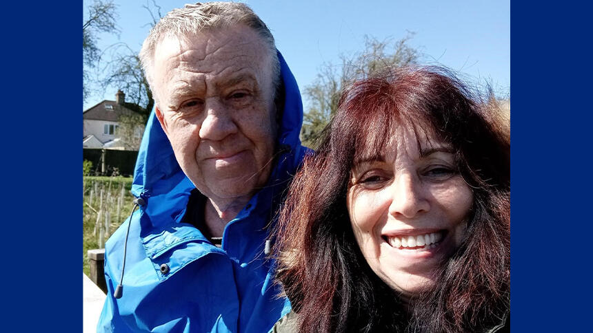 Man with white hair wearing a blue cagoule, woman to his right with brown hair smiling