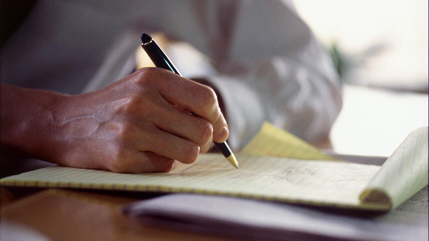 Hand holding a pen, writing on a notepad