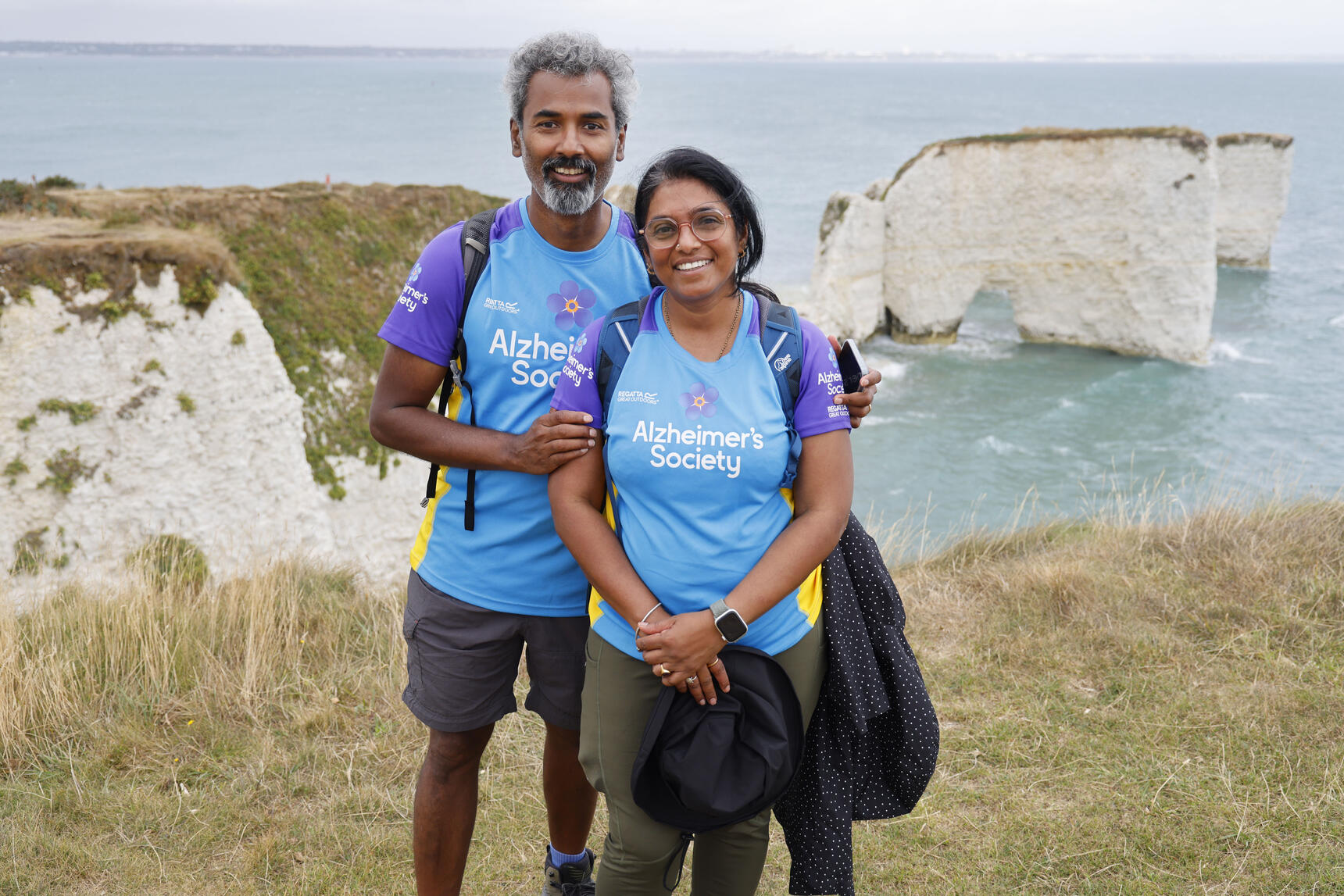 A couple stood by a cliff edge with white cliffs and the sea in the background.
