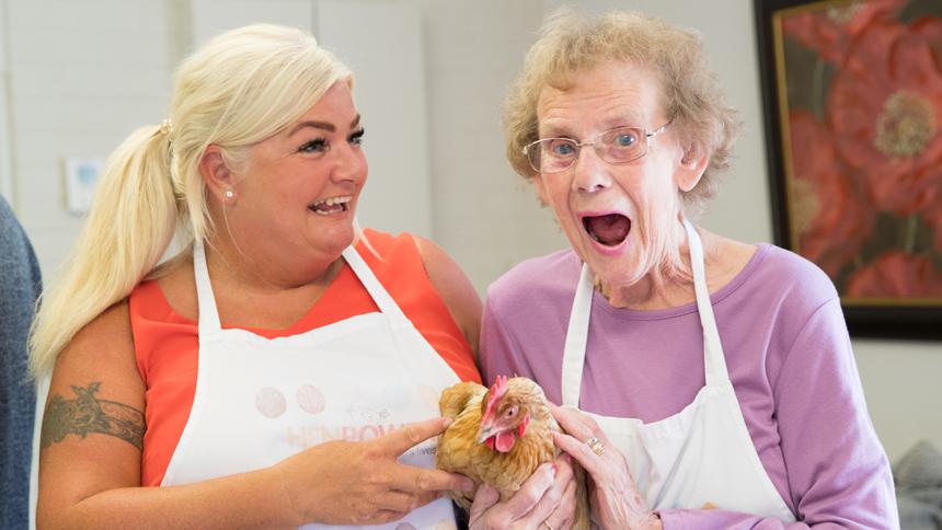 Two women holding a hen while smiling and laughing