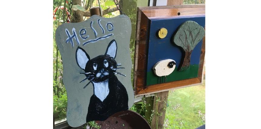 A painting of a cat saying hello next to a wooden picture of a sheep