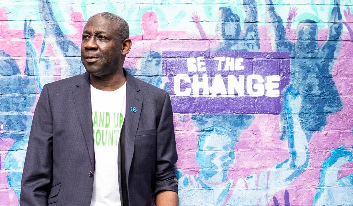 Ronald Amanze with graffiti that reads 'Be the change'